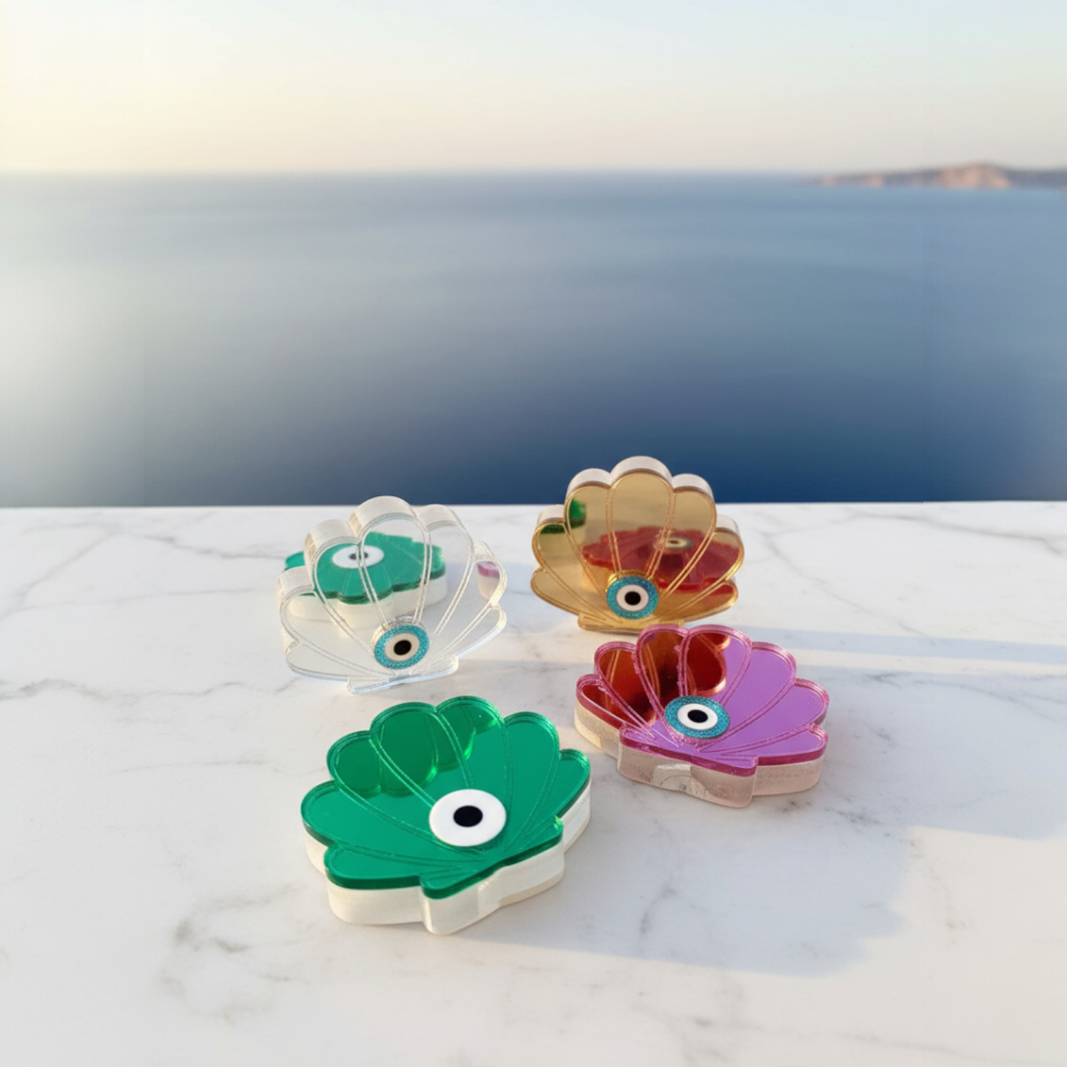 Χειροποίητο επιτραπέζιο γούρι κοχύλι με μάτι από πλεξιγκλάς καθρέφτη, τοποθετημένο σε λευκή μαρμάρινη επιφάνεια με φόντο τη θάλασσα και φυσικό μεσογειακό φως – So Cute by Dimi.