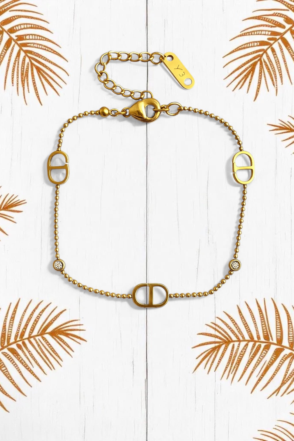 Ατσάλινο χρυσό βραχιόλι με ζιργκόν και διακοσμητικά στοιχεία σε σχήμα D, φωτογραφημένο σε λευκό φόντο.