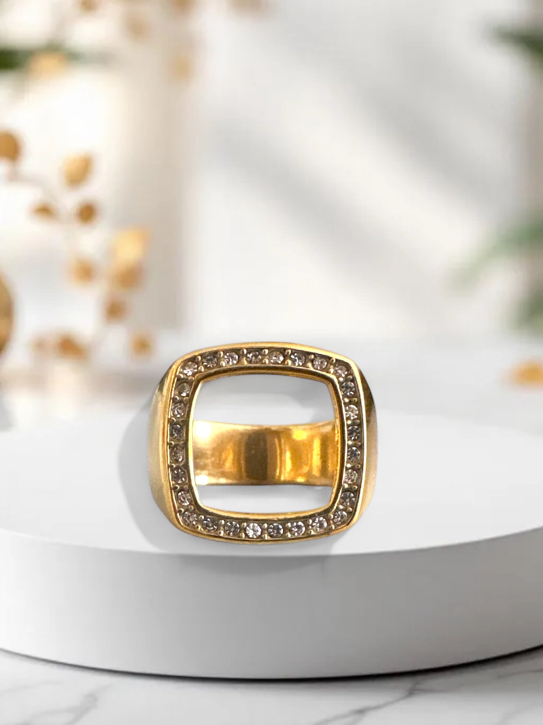 Χρυσό ατσάλινο δαχτυλίδι με λευκά ζιργκόν και γεωμετρικό άνοιγμα, σε μαρμάρινο φόντο.