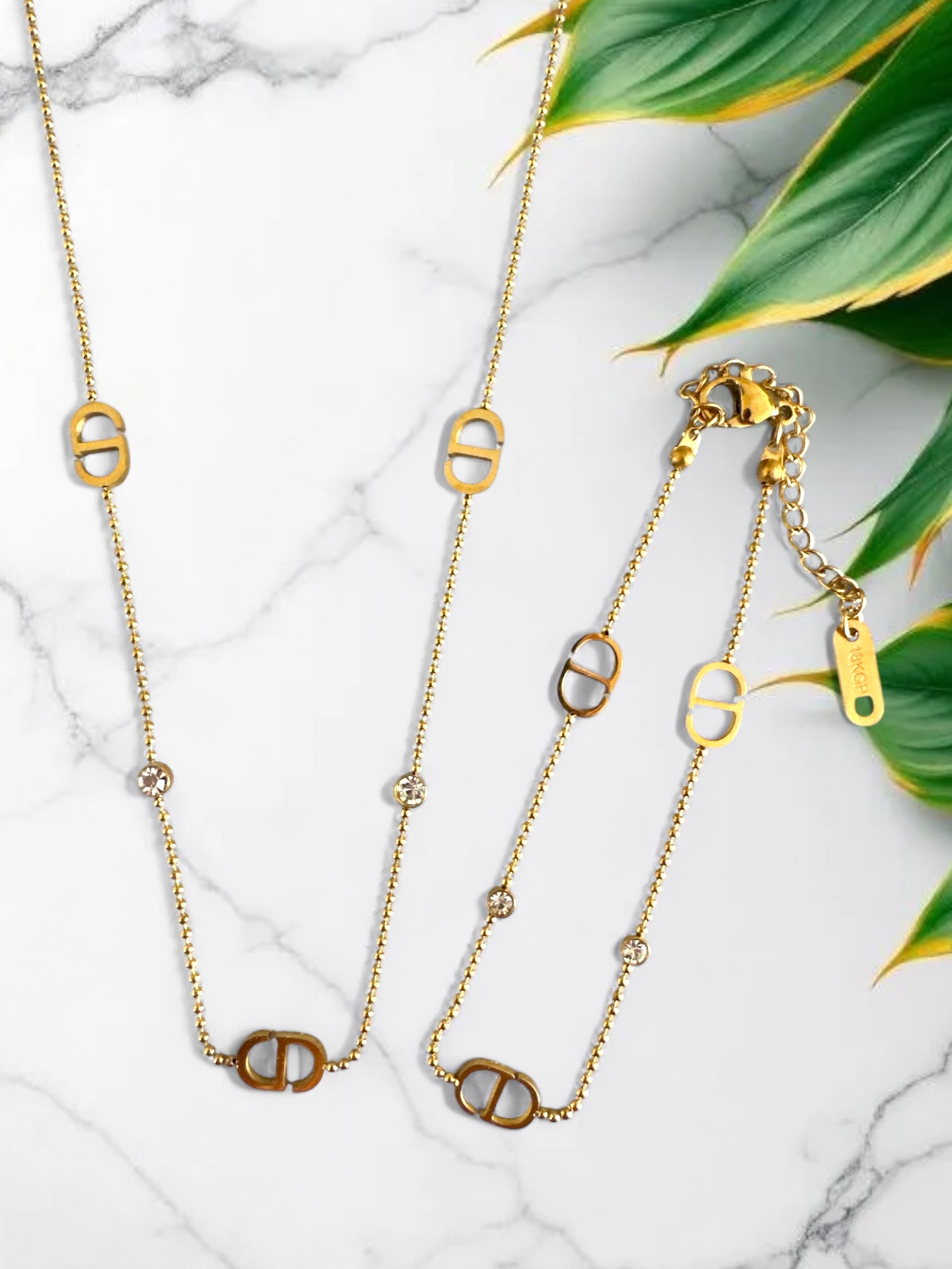 Ατσάλινο χρυσό κολιέ και  βραχιόλι με ζιργκόν και διακοσμητικά στοιχεία σε σχήμα D, φωτογραφημένο σε λευκό φόντο.