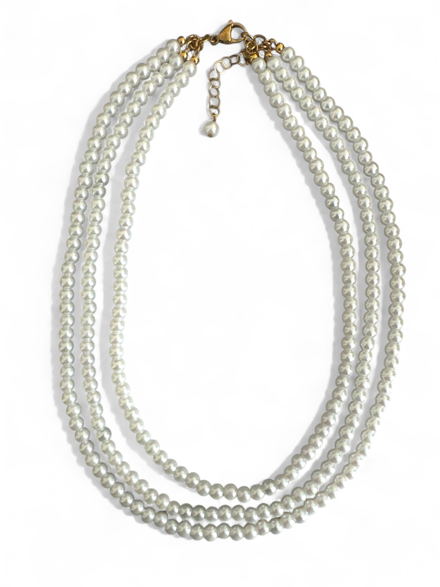 Τριπλό κολιέ με γυάλινες περλέ χάντρες σε διαβαθμισμένα μήκη και ατσάλινο κούμπωμα, σε λευκό φόντο.
