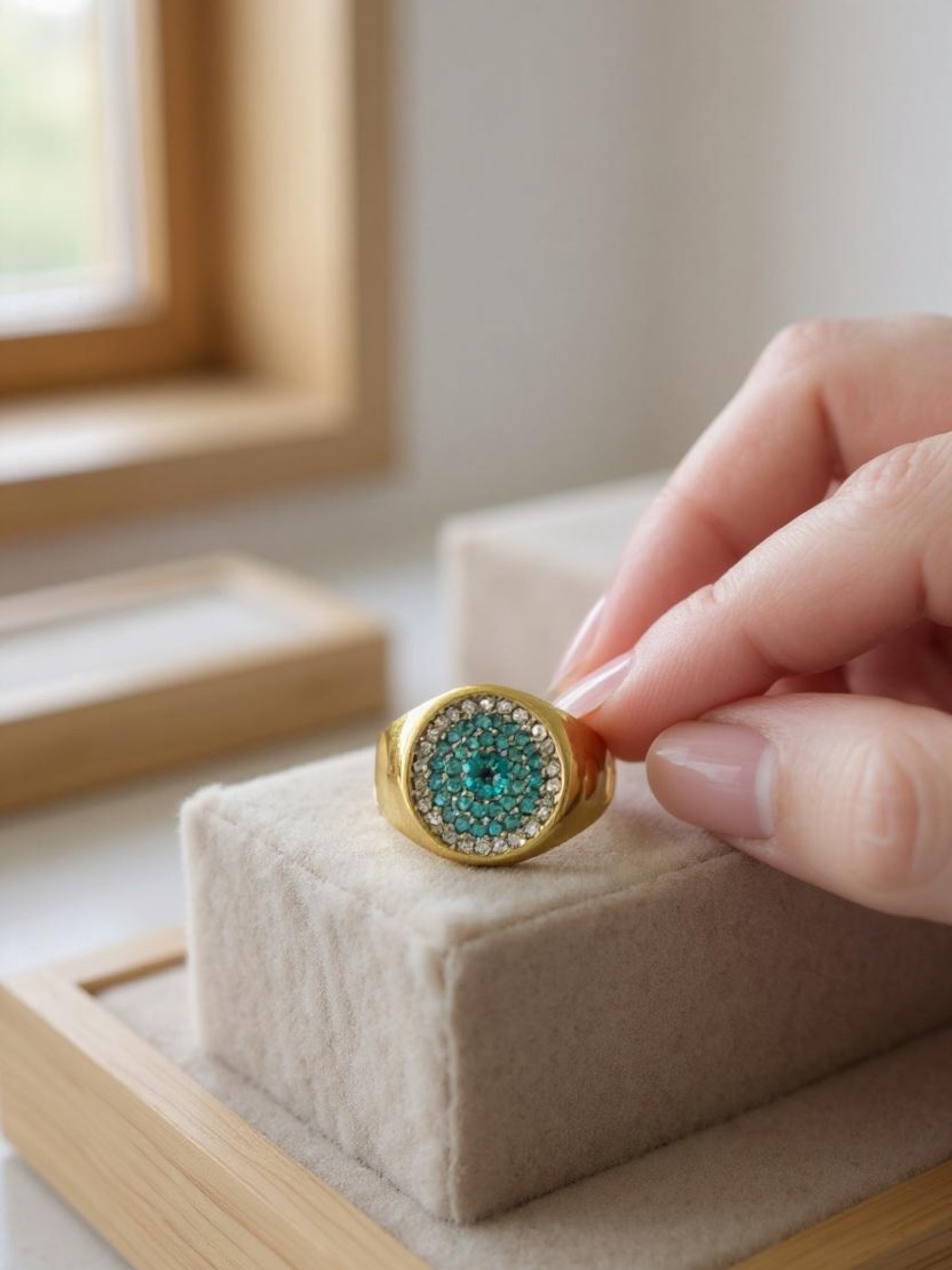 Gold ring with green gemstone on a jewelry display block, held by a hand.