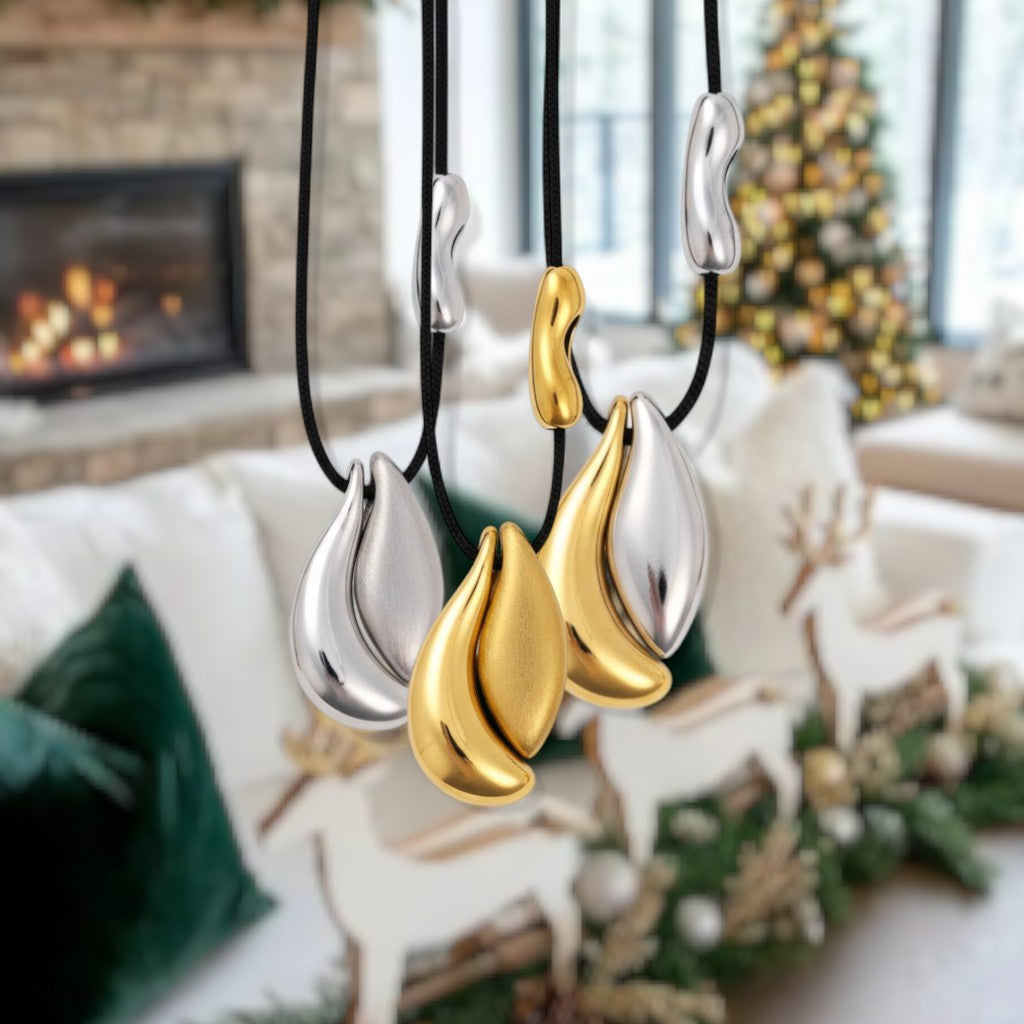 Three necklaces with teardrop pendants in gold and silver hanging against a festive background.