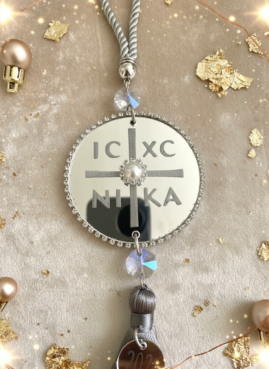 Ασημί γούρι IC XC NIKA σε κοντινή λήψη πάνω σε γιορτινό glam φόντο.