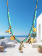 Necklace with gold and turquoise charms against a blue sky and white building background So Cute by DImi