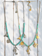 Two necklaces with turquoise beads and various charms on a wooden background So Cute by DImi