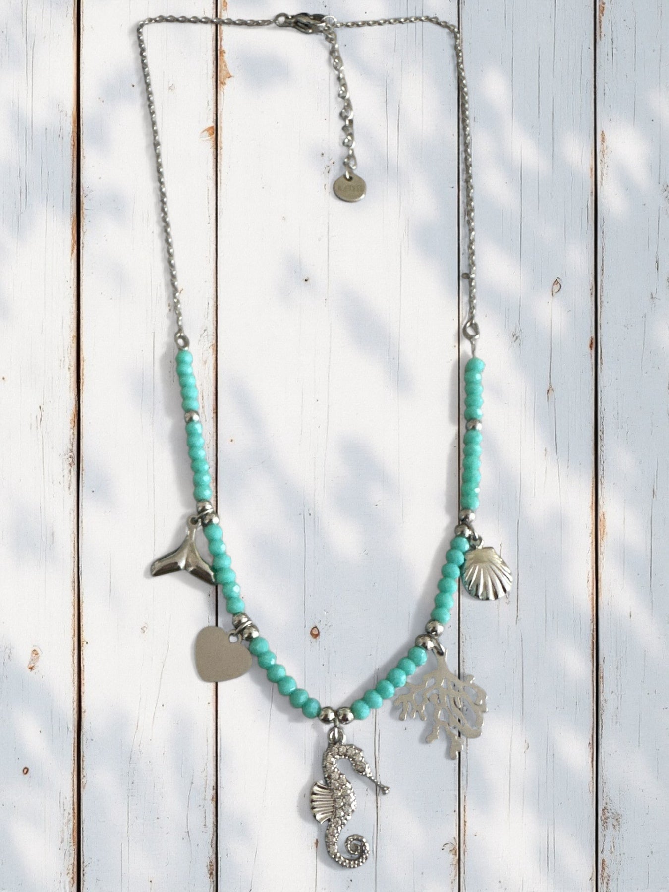 Necklace with turquoise beads and silver charms on a wooden surface So Cute by DImi