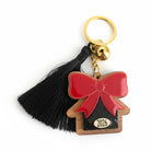 Χειροποίητο μπρελόκ γούρι 2026 με ξύλινο σπίτι, κόκκινο plexi φιόγκο, μαύρη φουντίτσα και χρυσό κουδουνάκι.