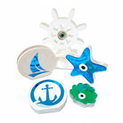 Χειροποίητα ναυτικά γούρια από πλεξιγκλάς σε λευκό φόντο — τιμόνι, άγκυρα, ιστιοφόρο, αστερίας και κοχύλι σε μπλε, λευκές και γαλάζιες αποχρώσεις, So Cute by Dimi.