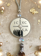 Ασημί γούρι IC XC NIKA σε κοντινή λήψη πάνω σε γιορτινό glam φόντο.