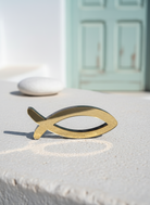 Χρυσό επιτραπέζιο ψάρι από πλεξιγκλάς σε κυκλαδίτικο σκηνικό με λευκούς τοίχους και κλαδάκι ελιάς